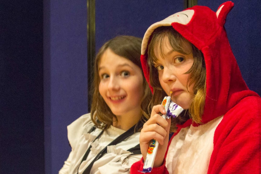 Two girls, one eating a chocolate bar.