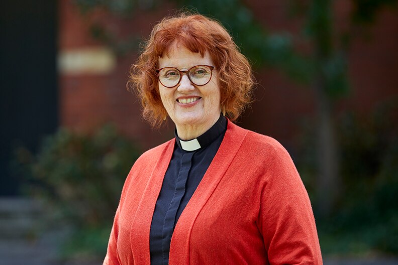 A woman with red hair wearing a priest's collar