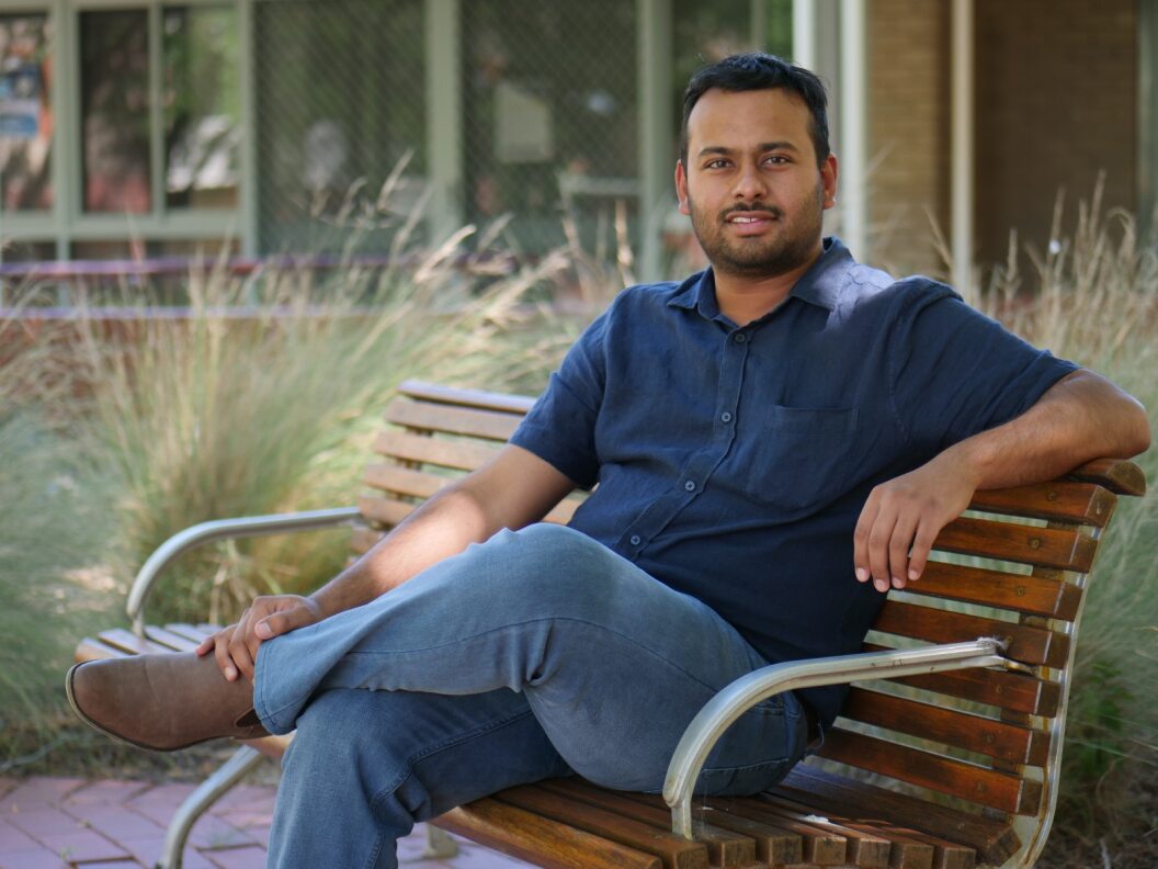 a man in a blue shirt and jeans sits on a park bench portrait