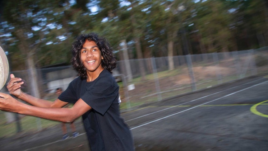 A boy in a black T-shirt passes a football while running past the camera,