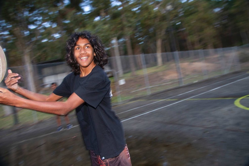 A boy in a black T-shirt passes a football while running past the camera,