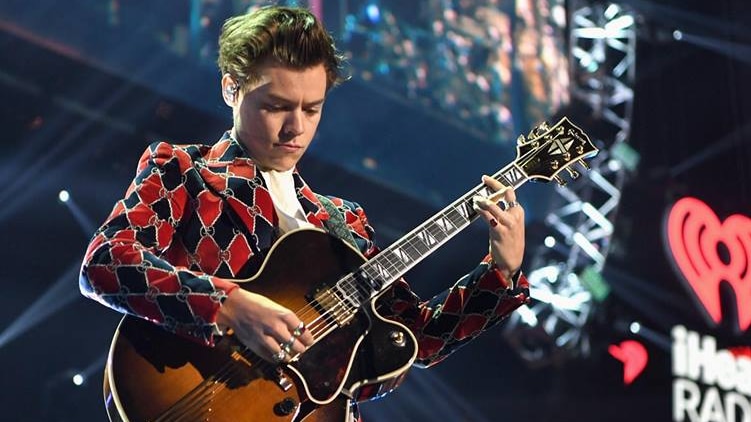 Harry Styles in a snappy suit with guitar.