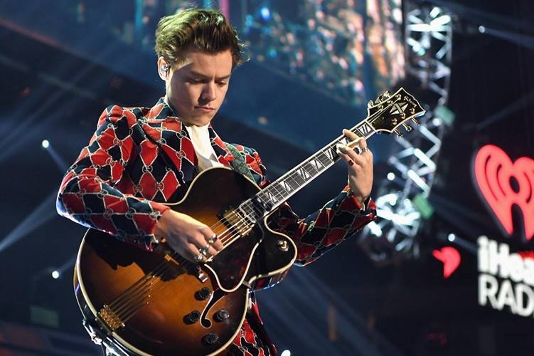 Harry Styles in a snappy suit with guitar.