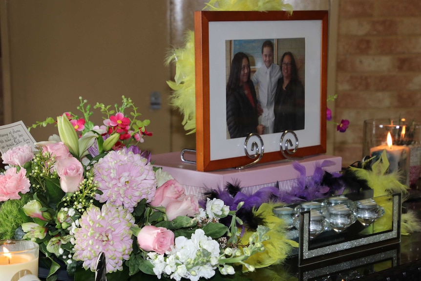 A photo of Michelle Peterson and her children Rua and Bella sits alongside flowers and lit candles.