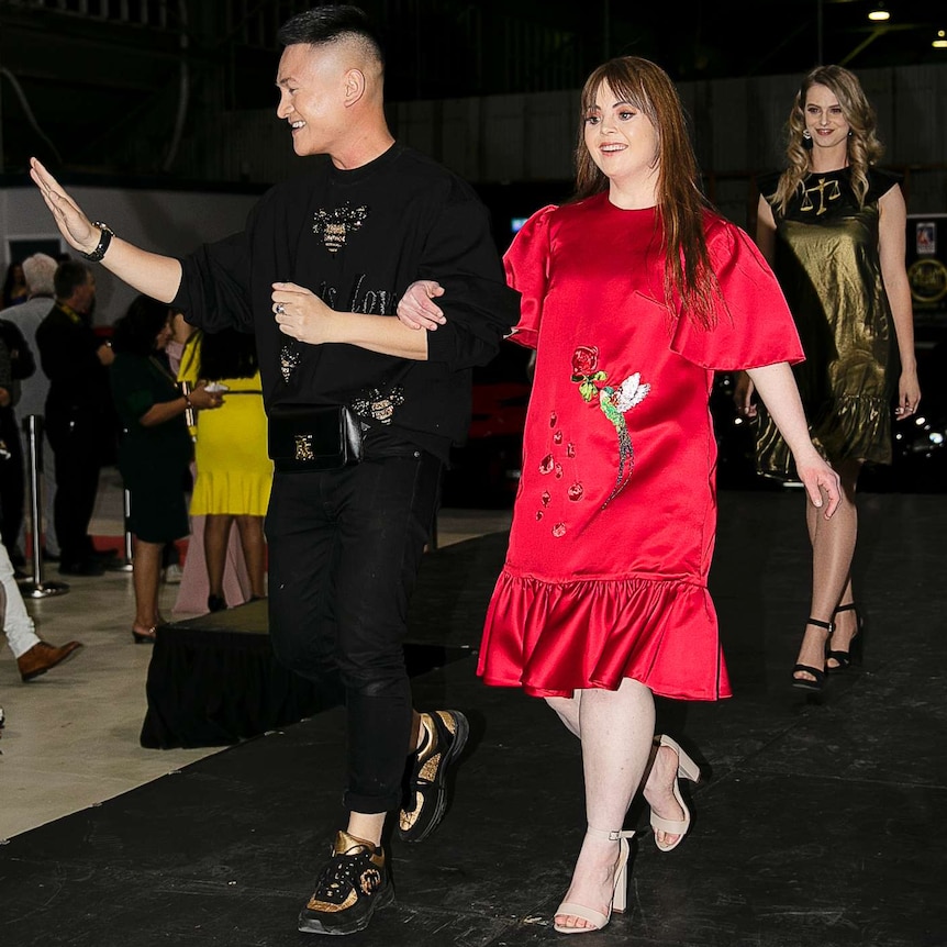 Woman in red dress arm-in-arm with a man walking on catwalk