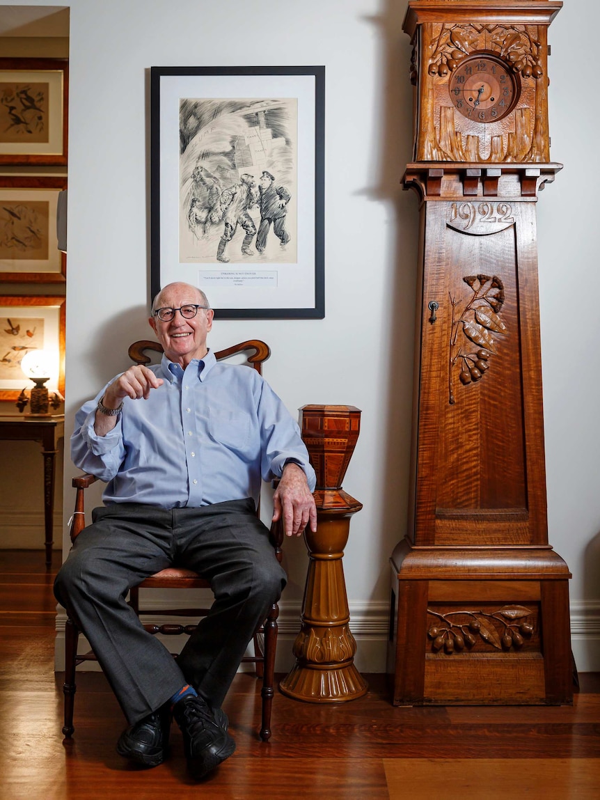 Trevor sits in an ornate carved chair next to an intricately designed wooden clock.