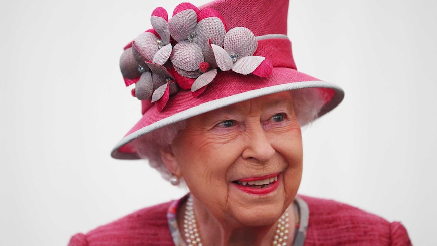 Queen Elizabeth II, wearing a pink floral hat, smiles for a photo.