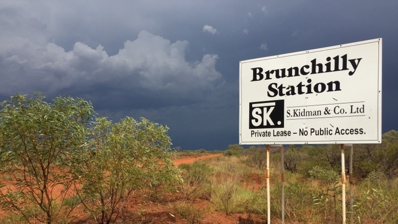 A sign reading "Brunchilly Station" on stilts in red dirt with green shrubs surrounding it.