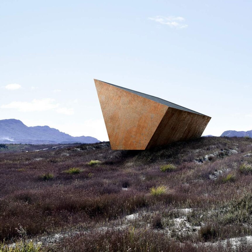 A trapezoid steel shape, rusted, sits cantilevered on a stone outcrop.