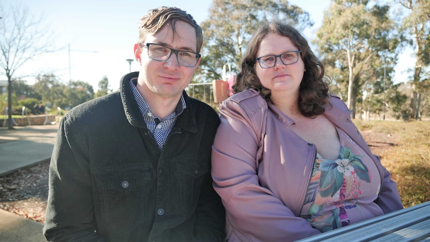 A man and a woman sit at a picnic table in a park.