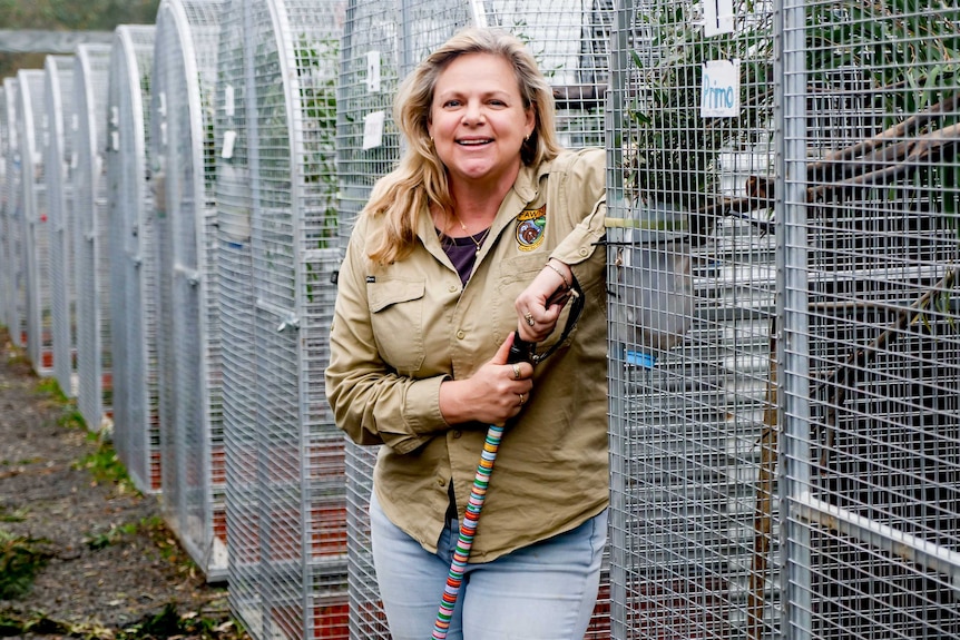 A blonde woman in a khaki shirt stands among the cages in an animal sanctuary.