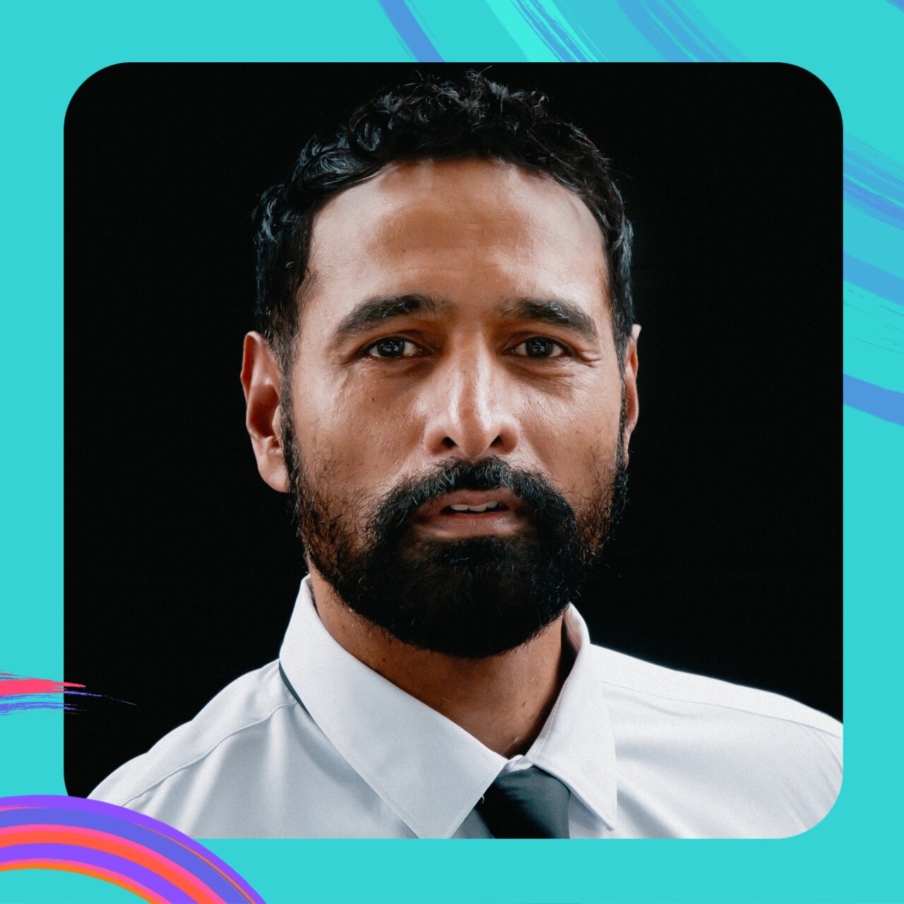 A studio portrait of Nicholas Brown, who has a dark beard and dark hair. He is wearing a white button up shirt.