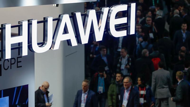 A neon logo of Huawei suspended above a passing crowd