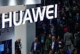A neon logo of Huawei suspended above a passing crowd.