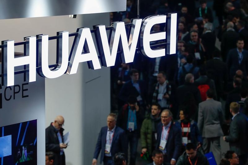 A neon logo of Huawei suspended above a passing crowd