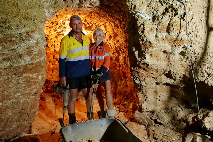 Gregg and Lynette in high visibility shirts holding tools, underground, light behind.