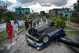 People walk down a Havana street devastated by a tornado, passing by a car flipped on its back on top of a crushed power pole
