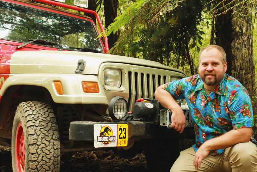 A man with short share sits in front of a jeep