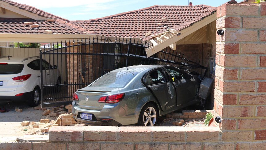 A greay car embedded in the front of a brick house after crashing into the building.