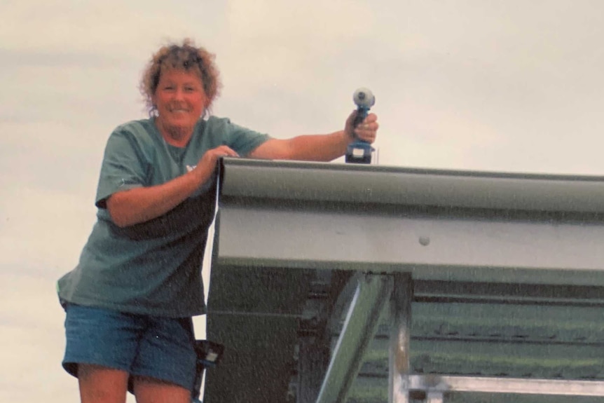 Judy Papp is standing on a ladder holding a power drill.