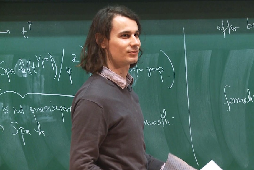 German mathematician Peter Scholze stands in front of a blackboard.