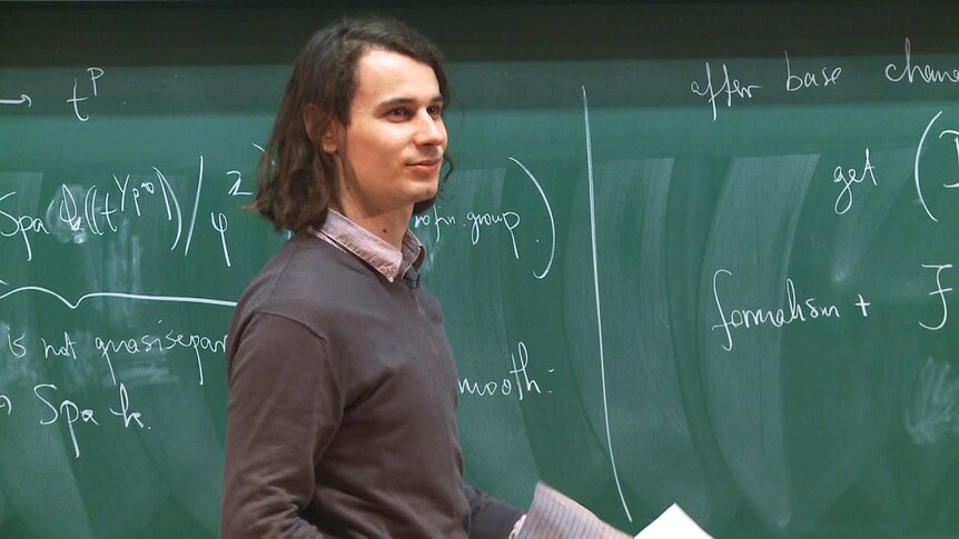 German mathematician Peter Scholze stands in front of a blackboard.