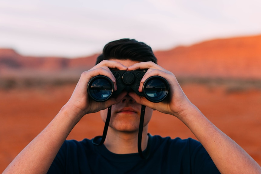 Man looking through binoculars in outdoor desert environment, depicting the research one should undertake before changing banks