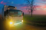 A milk truck drives through a rural area at dawn.