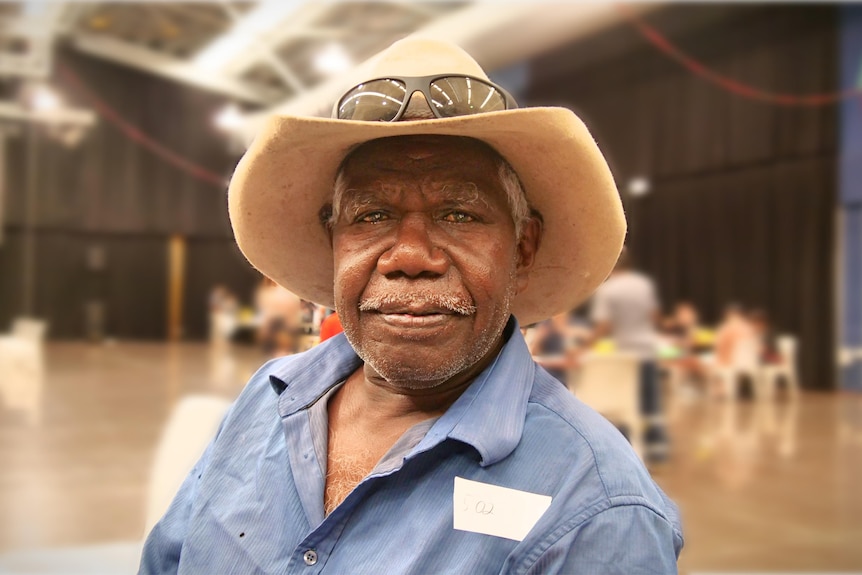 Aboriginal man wearing cowboy hat sits in big hall