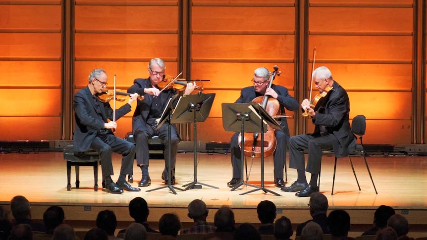 The four members of the Emerson String Quartet playing on stage in front of a timber-panelled wall