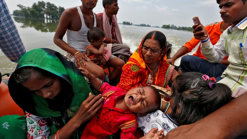 Adults and young children sit on a boat after being rescued from floodwaters.