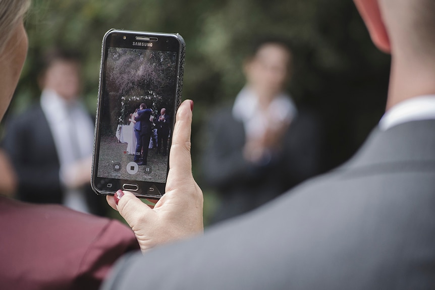 A wedding guest using a smartphone to capture a video of the bride and groom.