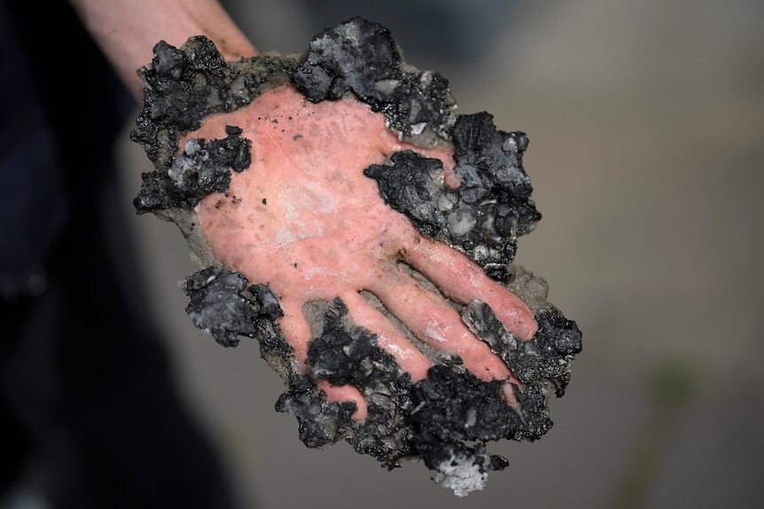 A close up of a hand caked in glue and black rocky tar from a road.
