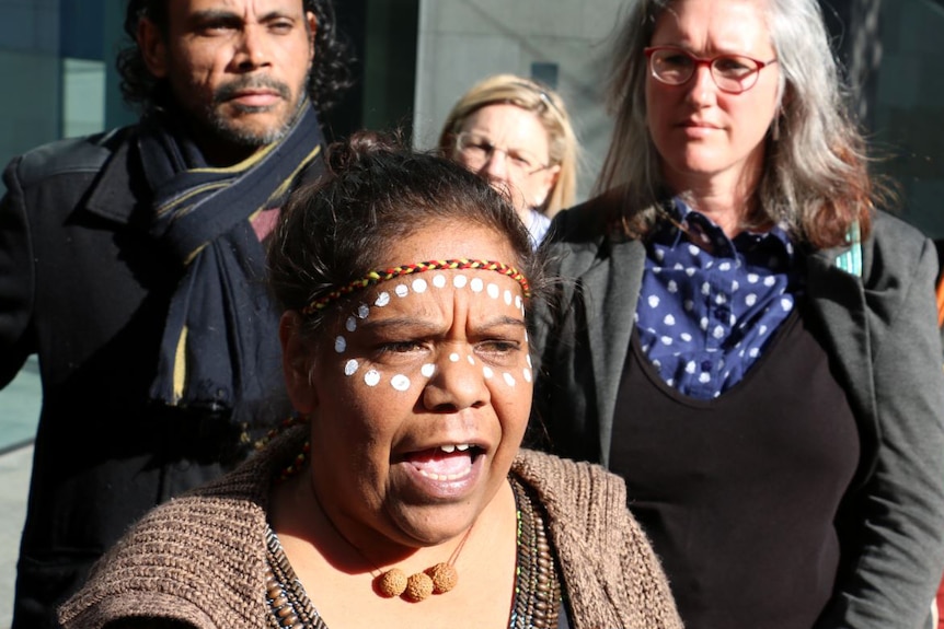 Corina Abraham, with her face painted with dots, with supporters outside court.