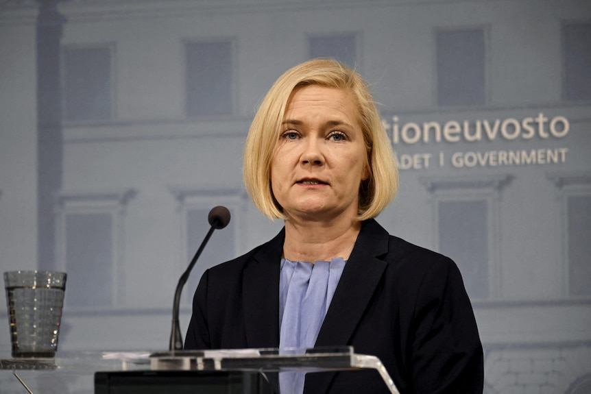 Mari Rantanen stands in front of a microphone wearing a silk blouse and a blaser