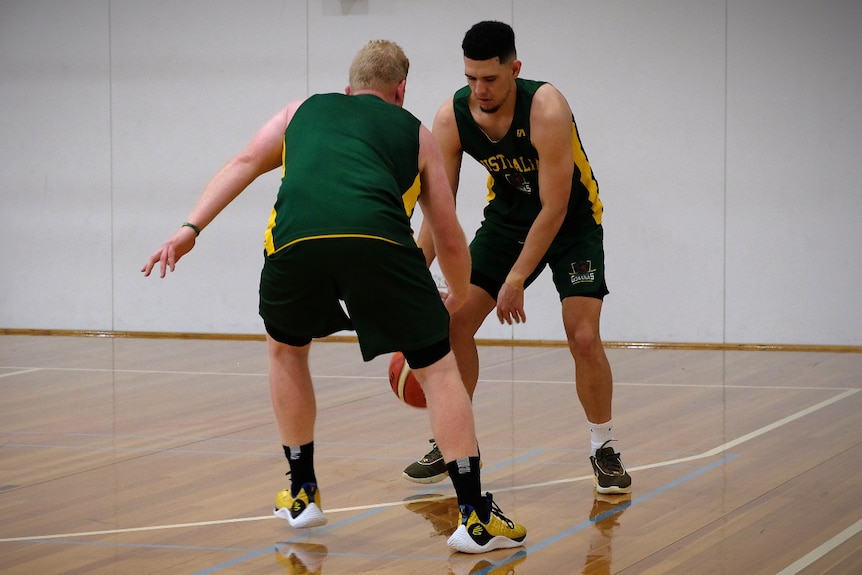 Two players in green Australia jerseys play one-on-one basketball on an indoor court.