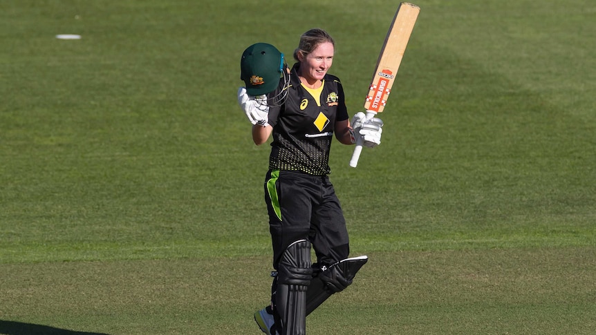 A cricketer raises her helmet and bat after scoring a century for Australia.