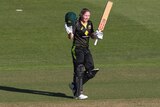 A cricketer raises her helmet and bat after scoring a century for Australia.