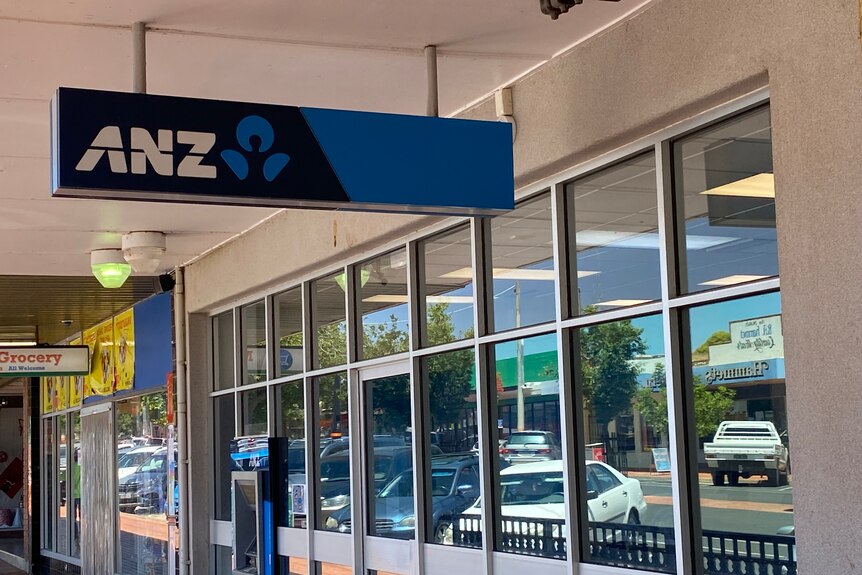 Blue and white ANZ Bank sign hanging outside bank and above a footpath