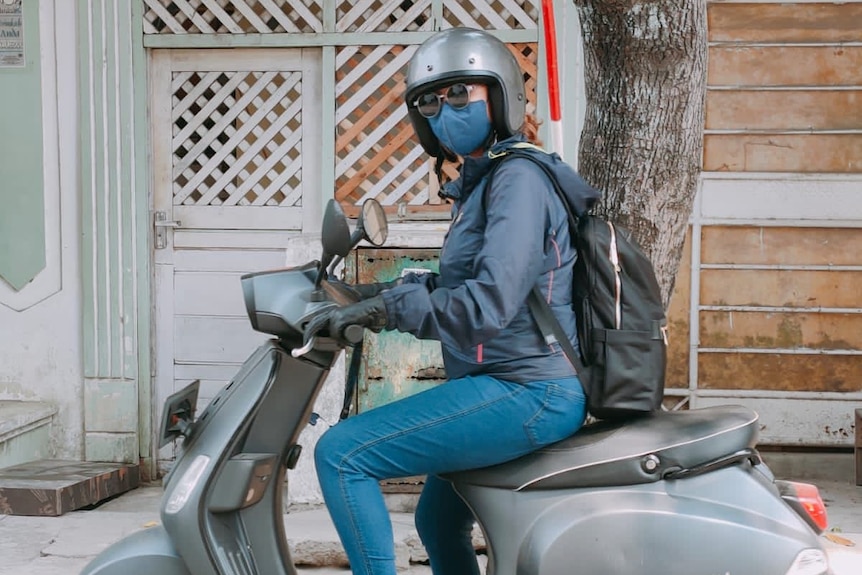 Woman wearing helmet, mask, and glasses on a motorbike.