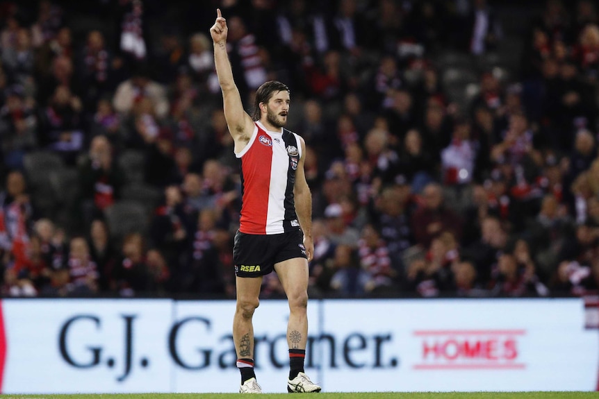 A male AFL player walks and points his finger in the air to celebrate kicking a goal.