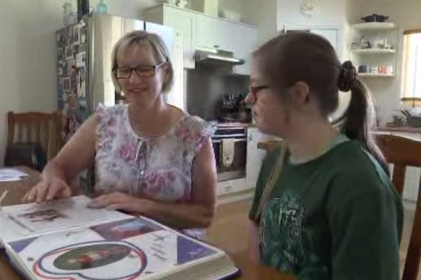 Two women sit at a table and look at a photo album.