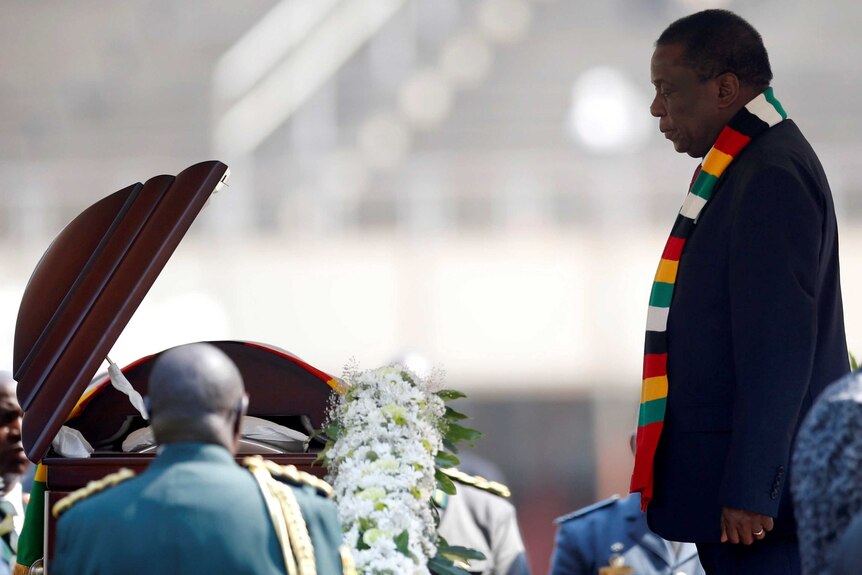 From a distance, you see the open coffin of Robert Mugabe as Emmerson Mnangagwa is beside it looking into it.