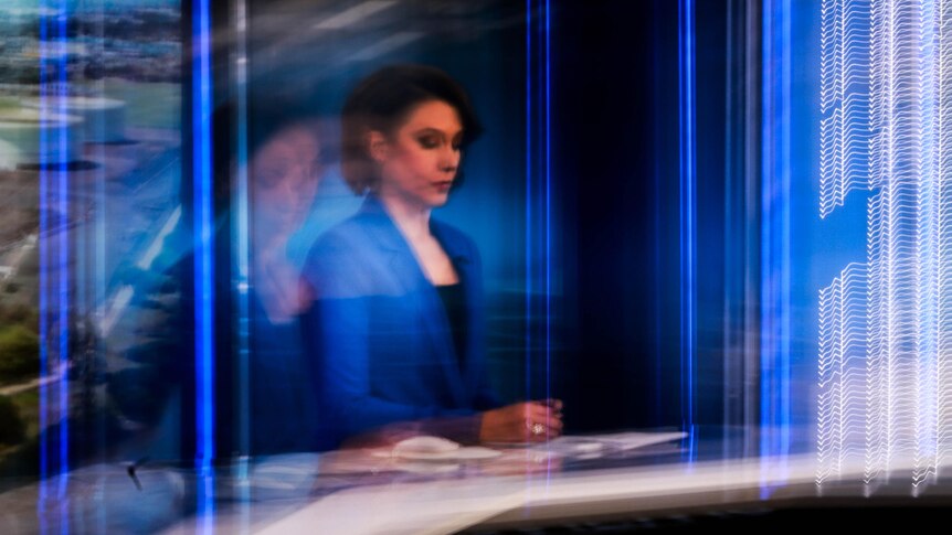 A long exposure creates a blurry and distorted image of Tamara Oudyn sitting at the ABC News desk in the studio.