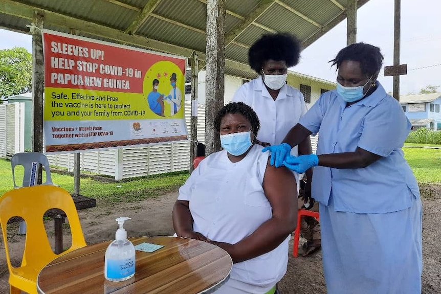 A Bougainville woman in a mask gets a needle in her arm from two nurses 