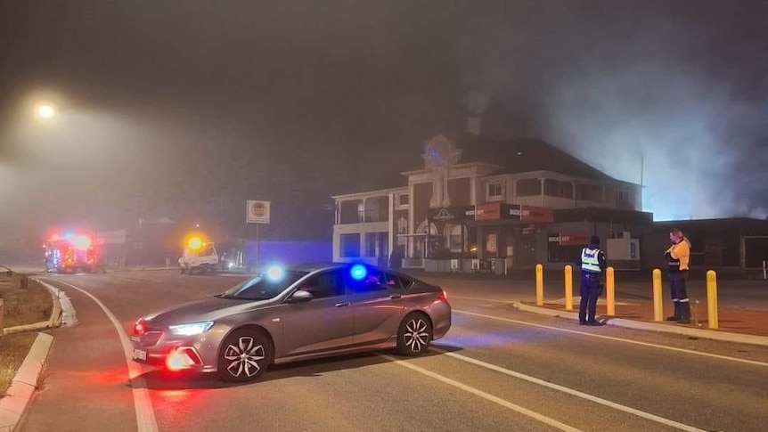 A car parked across the road with a hotel in the background with smoke coming out of it