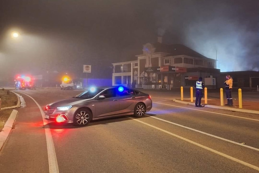 A car parked across the road with a hotel in the background with smoke coming out of it