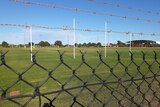 Barbed wire and mesh fence with grass and goal posts beyond