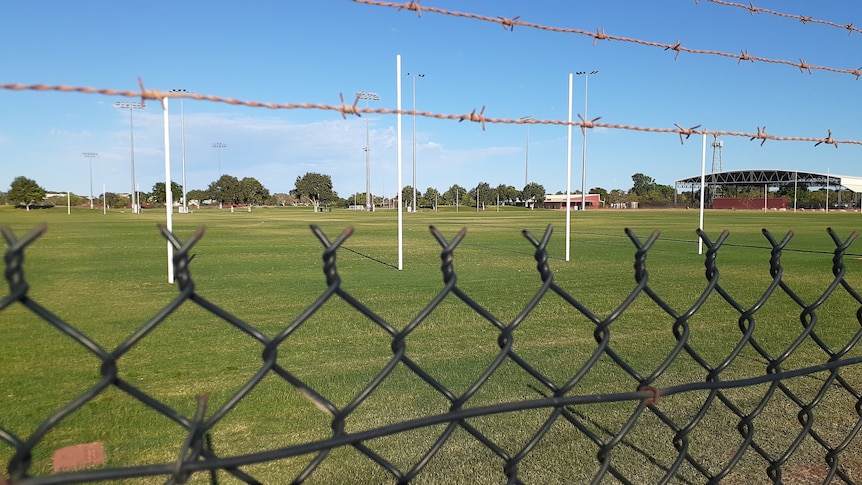 Barbed wire and mesh fence with grass and goal posts beyond