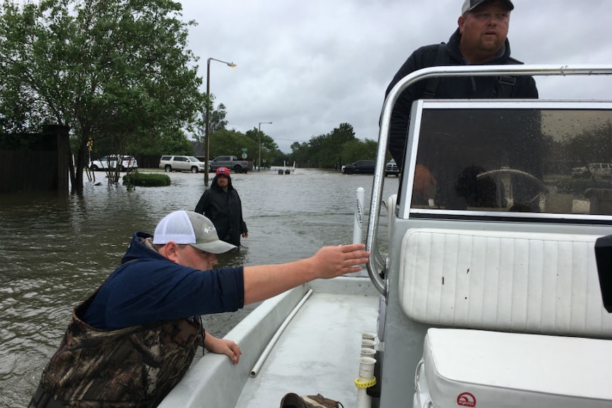 One man drives a boat as another wades alongside on a flooded street.